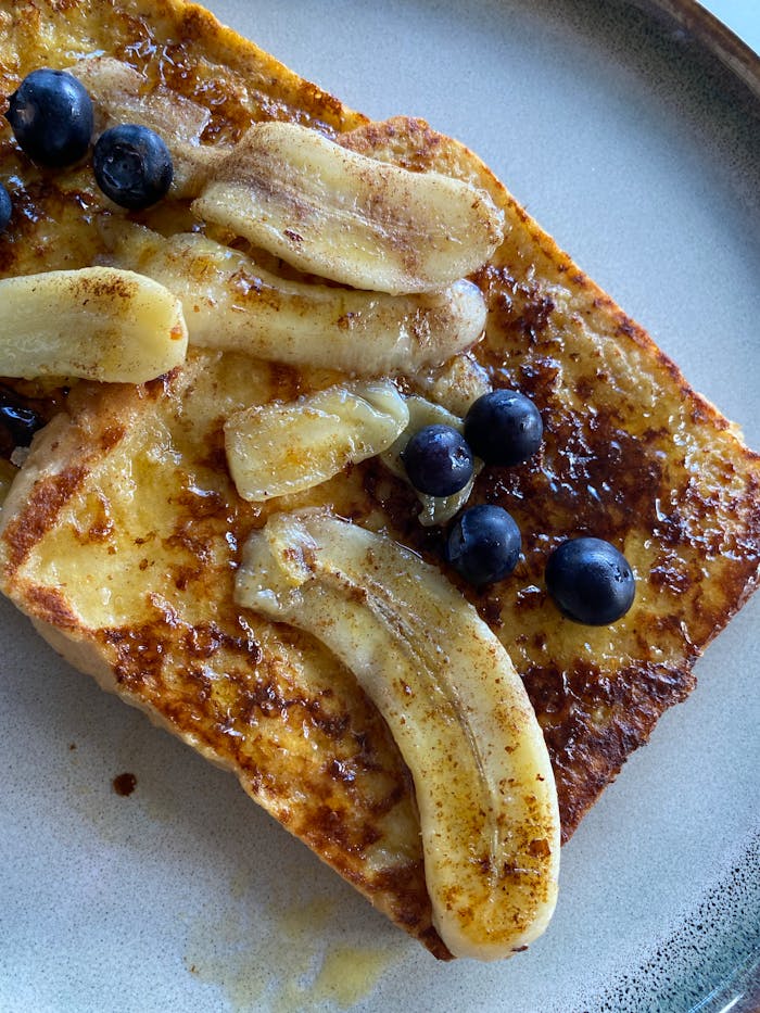 Home Close-up of French toast topped with sliced bananas and blueberries on a plate.