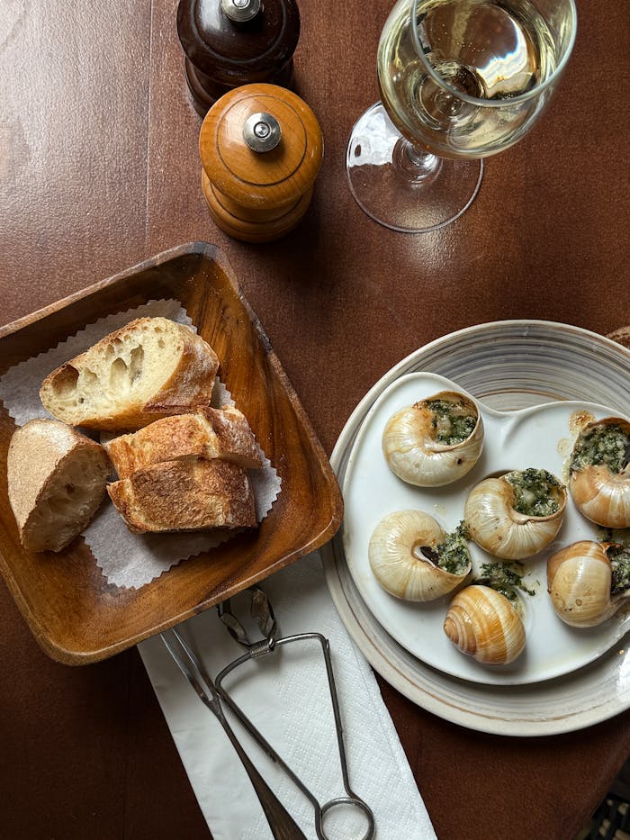 Menu Gourmet dining setup featuring escargot, bread, and white wine on a rustic table.