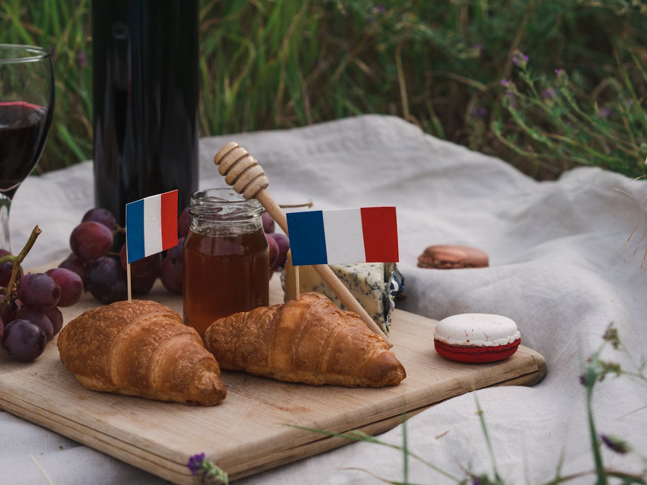 About A delightful French picnic setup with croissants, cheese, grapes, and red wine outdoors.