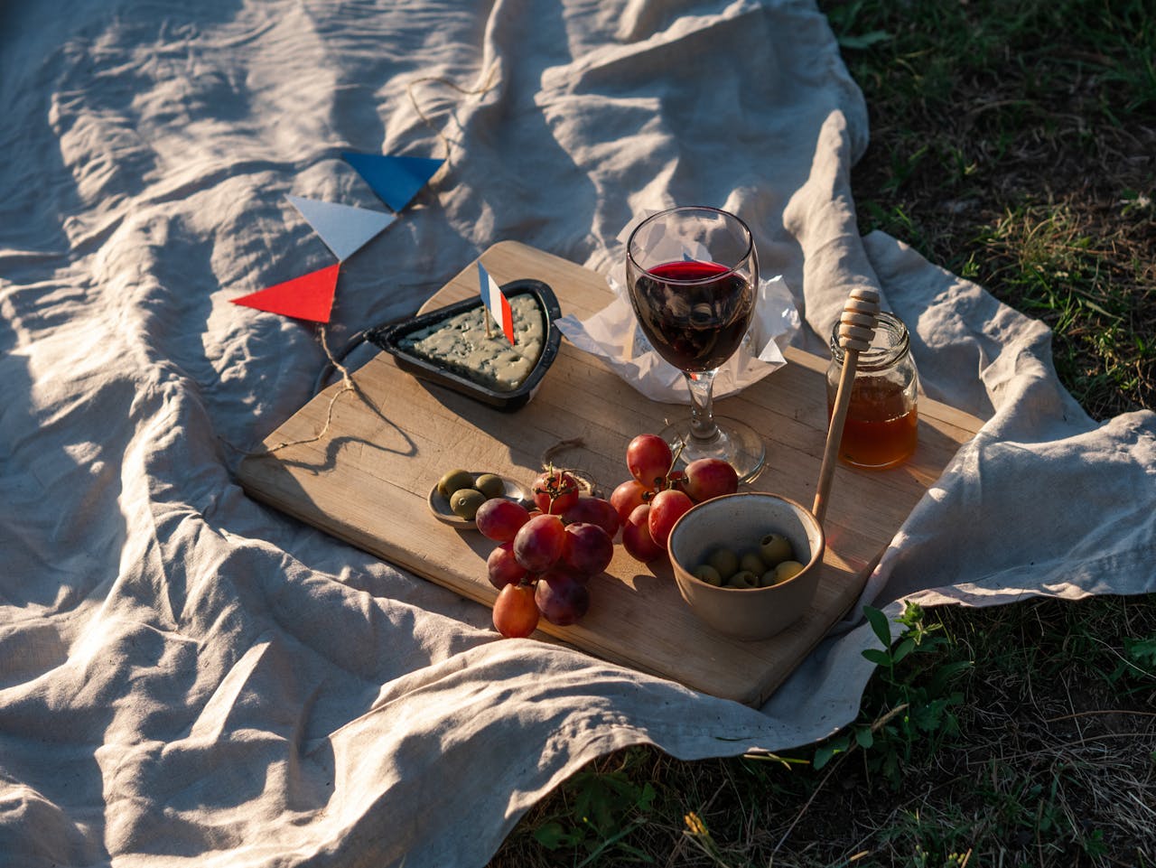 About A sunlit picnic setup with French wine, cheese, grapes, and honey outdoors.